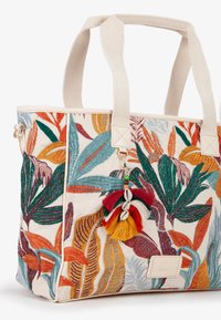 Bolso de mano bordado multicolor con lienzo crema, que presenta patrones de hojas, un charm de borlas y asas dobles. Los detalles incluyen un parche con el logo.