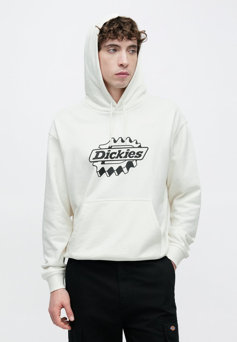 Felpa con cappuccio bianca con una tasca frontale e un logo nero sul petto. Dotata di cappuccio con coulisse e polsini a costine. Indossata con pantaloni neri.