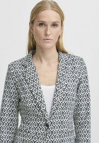 Patterovaný blejzr v modré a bílé barvě, s klopovým límcem, jedním knoflíkem a strukturovaným střihem s geometrickým vzorem.