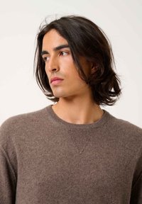 Brun stickad tröja med rund halsringning och texturerade detaljer vid axelsömmarna; mjukt material och en avslappnad passform.