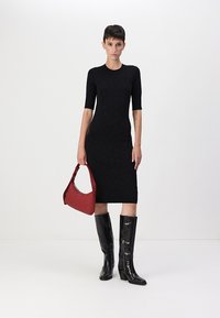 Abito in maglia nera con maniche corte, silhouette aderente, abbinato a una borsa rossa a spalla e stivali neri in vernice al ginocchio.