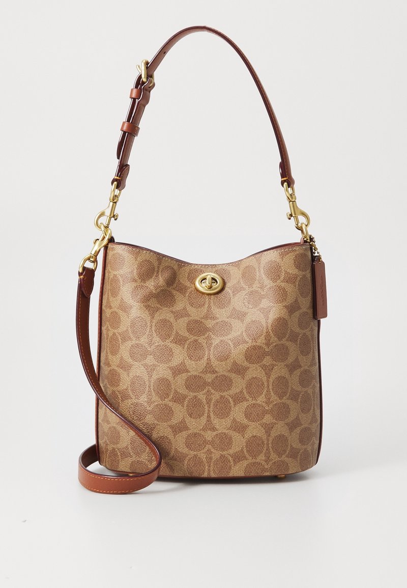 Sac à main en cuir marron à motif avec une sangle réglable, une fermeture à verrou tournant dorée et une étiquette en cuir suspendue sur fond blanc.