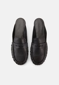 Ζευγάρι μαύρα δερμάτινα μοκασίνια χωρίς κορδόνια με στρογγυλεμένη μύτη και υφασμένες ακμές σόλας, φωτογραφισμένα από πάνω σε λευκό φόντο.