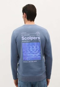 Blauwe sweatshirt met lange mouwen, voorzien van een grafische print van schedels en botten op de achterkant, en tekstdetails in contrasterende kleuren.