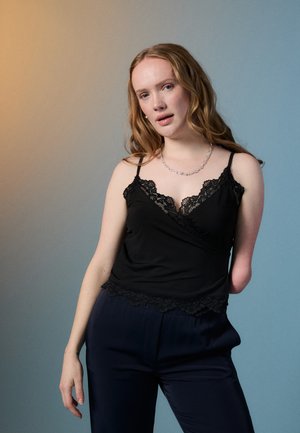 Camisola preta com renda nas bordas, apresentando alças finas e um design em estilo envoltório. Combinada com calças azul marinho escuras. Textura de tecido suave.