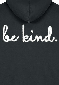 Črna kapuca z velikim belim vezenim napisom "bodi prijazen" na hrbtni strani. Gladka tekstura s kapuco in minimalističen dizajn.