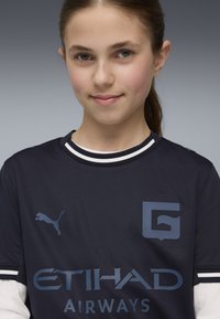 Mørkeblå sportstrøje med hvidstribede krave, prydet med et Puma-logo og "ETIHAD AIRWAYS" i lys blå skrift.