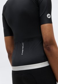 Οπίσθια όψη ατόμου που φορά στενό μαύρο ποδηλατικό μπλουζάκι με κοντά μανίκια, λευκή ζώνη στη μέση και λογότυπο "Castelli" στο κάτω μέρος της πλάτης.