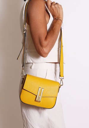 Sac bandoulière en cuir jaune avec une finition texturée, quincaillerie dorée et fermeture à rabat. Il dispose d'une longue sangle réglable et d'un contour contrastant.