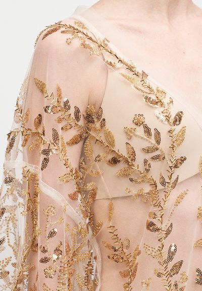 Διάφανο μπεζ ύφασμα με κεντήματα φύλλων από χρυσές παγιέτες και λεπτομέρειες από μεταλλικό νήμα. Ελαφρύ, ρέον σχέδιο με λεπτή, υφήλιστη υφή.