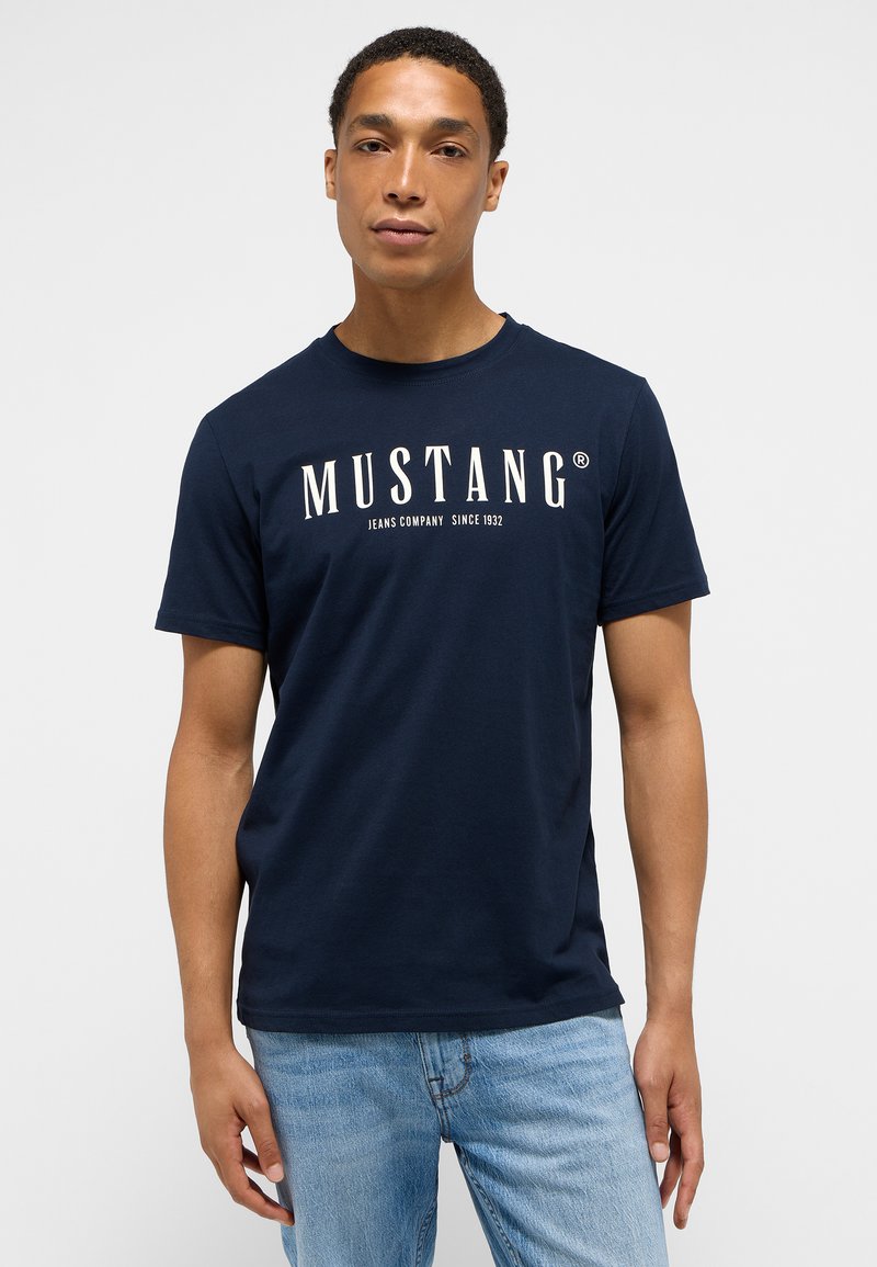 Tmavě modré tričko s krátkým rukávem vyrobené z bavlny, s bílým logem a textem "MUSTANG". Jednoduchý styl s kulatým výstřihem, hladká textura.