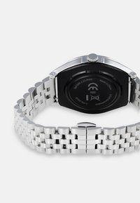 Reloj de acero inoxidable plateado con una pulsera texturizada y un fondo de caja negro. Presenta una corona prominente y un cierre de hebilla.