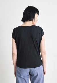 Top preto de mangas curtas com uma textura listrada subtil, apresentando um decote em forma de barco e um corte relaxado, combinado com calças azul claro.