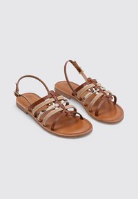 Sandalias de cuero marrón con correas de tela trenzadas, punta abierta y hebilla en el tobillo. Suela plana con un acabado suave y textura natural.