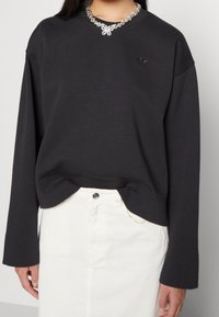 Black sweatshirt with oversized sleeves, designed with a round neckline and embellished collar. Paired with a white skirt.