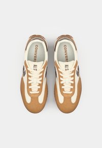 Bežiniai ir rudi sportbačiai su zomšiniu ir kanvos viršumi, su baltomis raištelėmis ir "CONVERSE ALL STAR" užrašu auksinės spalvos ant vidpadžio.