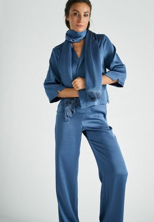 Blauw satijnen outfit met een cropped jas met wijde mouwen en bijpassende wijde pijpen broek. Gecombineerd met een sjaal met franjes.