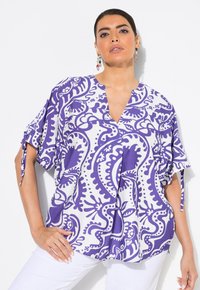 Top a fiori viola e bianchi con scollatura a V, vestibilità morbida, maniche corte e dettagli a fiocco sulle maniche. Tessuto dalla superficie liscia.