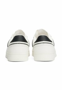 Zapatillas de cuero blancas con un acento negro en el talón, de superficie suave y suela de goma blanca con marca. Diseño minimalista, estilo bajo.