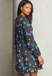 Blumenkleid mit schwarzem Hintergrund, blauen Rosen und weißen Punkten. Lange Ärmel, elastischer Bund und Schleifendetail auf der Rückseite.
