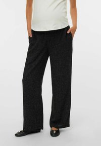 Hlače širokih hlačnic iz teksturirane črne tkanine z nežnimi pikčastimi vzorci. Imajo stranske žepe, kombinirane s svetlim zgornjim delom in črnimi čevlji.