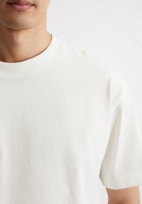 T-shirt met korte mouwen en ronde hals in crèmekleurige stof. Soepele textuur met een geribbelde halslijn en een relaxed fit.