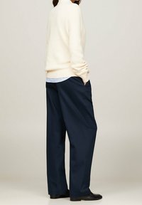 Light cream ribbed sweater paired with loose-fitting navy trousers. Trousers feature side pockets and a smooth fabric texture. Black shoes.