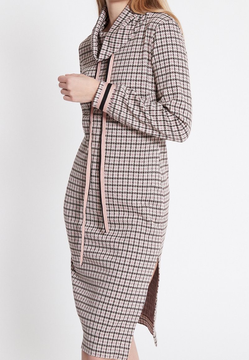 Robe à carreaux rose et noir, avec un décolleté en cowl, des manches longues, des fentes latérales et un cordon de serrage avec des accents contrastants.