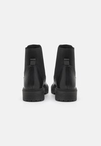 Botines negros con cuero suave y paneles elásticos, con una suela de goma texturizada y tiradores en la parte trasera para ponerse con facilidad.