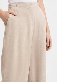 Beige wide-leg trousers made of textured fabric, featuring side pockets and a relaxed fit. Smooth finish with subtle pattern detail.