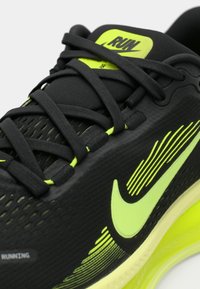 Gros plan d'une chaussure de course noire avec virgule Nike jaune fluo, lacets et détails de design sur le côté et la languette marqués "RUN".