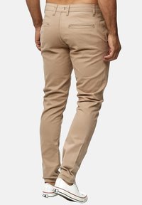 Chinos beige con vestibilità slim, dotati di tasche posteriori e una trama liscia. Abbinati a sneakers bianche, che mostrano un design minimalista.