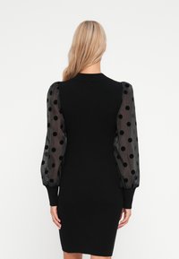 Abito nero a coste con lunghe maniche puff trasparenti decorate con pois neri. Design aderente con scollatura tonda e polsini aderenti.