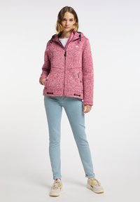 Rosa texturerad zip-up jacka med huva, dragsnören och fickor. Kombinerad med ljusblå jeans och neutrala gympaskor.