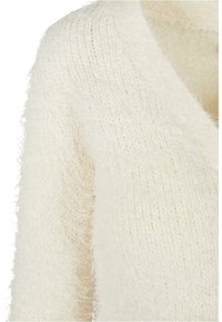 Gros plan d'un pull en maille duveteuse de couleur crème montrant la texture et la couture de l'épaule.