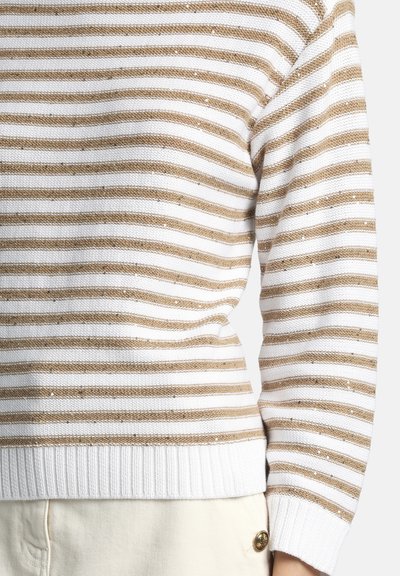 Pull à rayures horizontales beiges et blanches avec poignets et ourlet côtelés, porté avec un pantalon couleur crème orné d'un bouton décoratif.