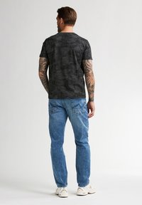 Černé tričko s krátkým rukávem s texturovaným vzorem stromů, sp paired with světlými modrými džíny a bílými teniskami.