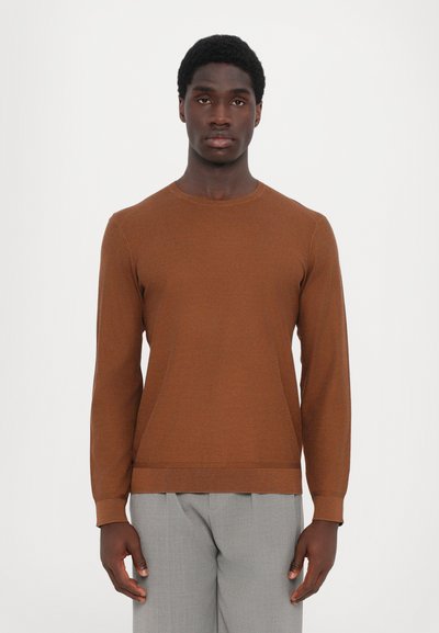 Maglione marrone a girocollo con maniche lunghe, realizzato in tessuto a maglia testurizzata. Abbinato a pantaloni grigi chiari sartoriali.