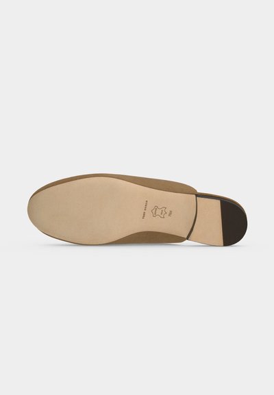 Semelle d'une chaussure habillée en cuir beige avec un embout de talon noir et un tampon qualité cuir au centre.