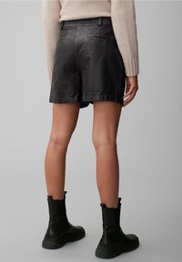 Černé kožené kraťasy s hladkou texturou, mírně volným střihem a zadními kapsami, doplněné černými kotníkovými botami. Náhlý lem na stehně.