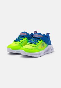Grønne og blå joggesko med mesh-overdel, snøring og trekkstrop. Hvit såle med mønstrede spor, som har "SKECHERS LIGHTS" merking.