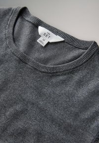 Sivi sivi džemper s okruglim izrezom i rebrastim rubovima, s etiketom na kojoj piše "THE SET", veličine M, proizveden u Bangladešu.