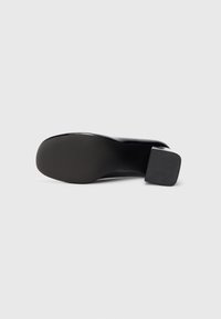 Pantof cu toc mic din piele lăcuită neagră, cu o bază din cauciuc pentru aderență. Suprafață netedă și design cu vârf rotunjit.