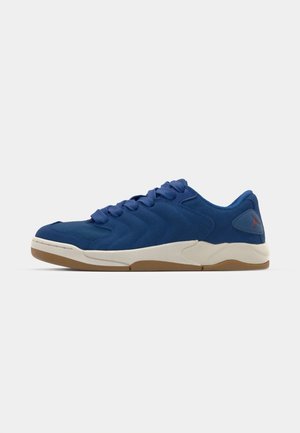 Blaue Sportschuhe mit strukturiertem Obermaterial, featuring eine Gummisohle und geschwungenem Design. Die Schnürsenkel sind durch gepolsterte Ösen geflochten. Rotes Logodetail an der Ferse.