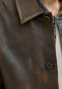 Dark brown leather jacket featuring a textured finish, large collar, and contrasting buttons with visible stitching.