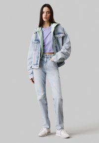 Chaqueta de mezclilla azul claro sobre una sudadera verde menta, acompañada de una camiseta lila y jeans azul claros. Zapatillas blancas completan el look.