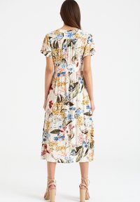 Blommig midiklänning med krämfärgad bakgrund, korta ärmar och en rynkad baksidedesign med flerfärgade blommönster.