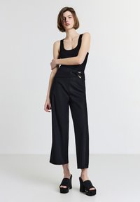 Canotta nera aderente abbinata a pantaloni neri larghi a vita alta con un dettaglio a fiocco e hardware dorato. Scarpe con plateau nere completano il look.