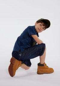Chemise bleue avec motifs texturés, shorts en jean et bottes laces de couleur tan avec semelles en caoutchouc, mettant en valeur un design robuste.