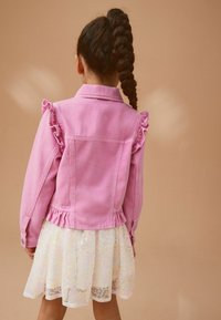 Veste en denim rose avec des accents de manches volantées et une taille élastique, associée à une jupe blanche ornée d'un motif floral scintillant.